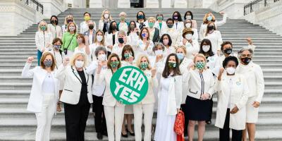 Democratic women celebrate passage of H.J.Res. 17 on U.S. Capitol steps. holding signs that reads, "ERA NOW!"